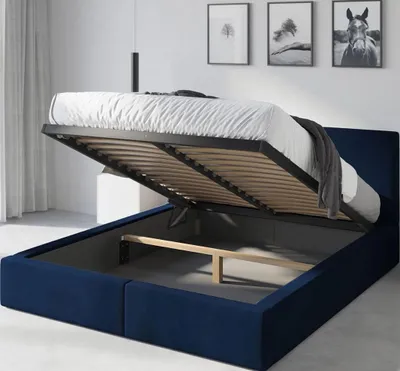 A blue upholstered bed frame with the mattress base lifted to reveal the storage space underneath.