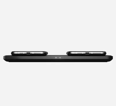 A black wireless charging pad with two smartphones on top, shown from a side view against a white background.