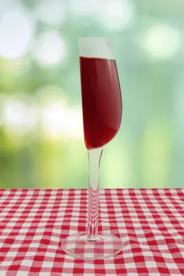 A half-filled wine glass sits on a red and white checkered tablecloth, with a blurred green background.