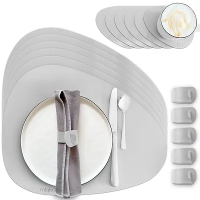 A set of gray placemats with a plate, napkin, and cutlery arranged on one of them. There are also several napkin rings and a stack of placemats in the background.