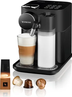 A black Nespresso coffee machine with a glass of latte and a milk carafe, along with coffee capsules and packaging.