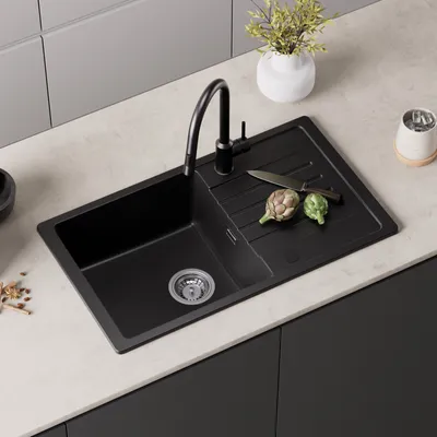 A black granite kitchen sink with a black faucet and a cutting board with two artichokes and a knife on a light-colored countertop.