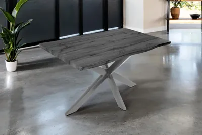 A dining table with a wooden top and a spider-like metal base is shown in a room with a concrete floor.