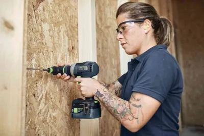 A woman is using a cordless drill to drill a hole in a wooden wall.