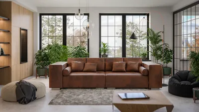 A spacious living room with a large brown sofa, plants, and large windows.