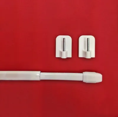 A white adjustable rod and two white adhesive hooks are laid out on a red background.