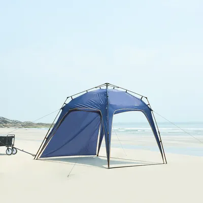A blue beach tent set up on a sandy beach with the ocean in the background.