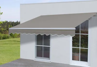 An awning is installed over two windows on the exterior of a white building, with a grassy yard and trees in the background.