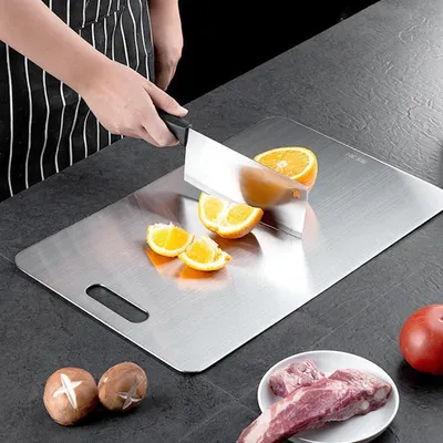 A person is cutting oranges on a stainless steel cutting board, with mushrooms and meat in the foreground.