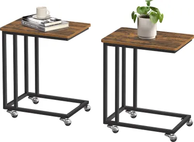 Two C-shaped side tables with a vintage brown wood top and black metal frame, each with wheels. One table has books and a mug on it, the other has a potted plant.
