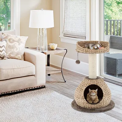 A cat tree is placed in a living room next to a sofa and a side table with a lamp.