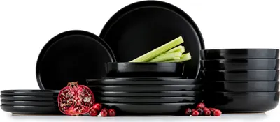 A set of black ceramic dishes, including plates and bowls, arranged on a white background. A pomegranate and cranberries are placed in the foreground.