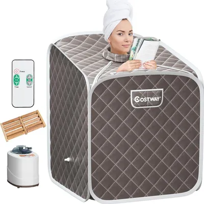 A woman is sitting inside a portable sauna, reading a book. The sauna is set up in a studio environment with other accessories shown around it.