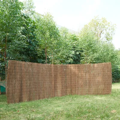 A woven reed fence is displayed in a grassy outdoor setting with trees in the background.