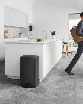 A person walks past a black kitchen trash can in a modern kitchen.