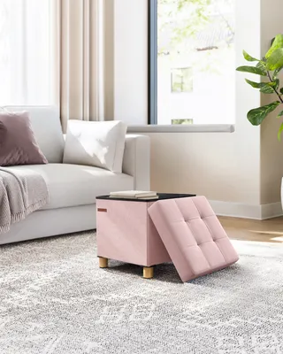 A pink ottoman with a lifted lid sits on a patterned rug next to a white sofa.