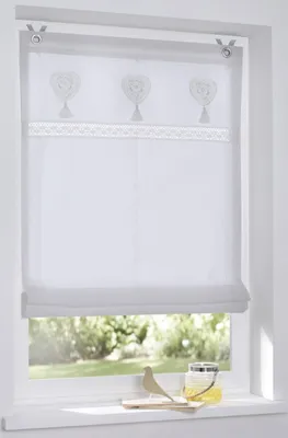 A white Roman blind with embroidered hearts and tassels is shown hanging in a window.
