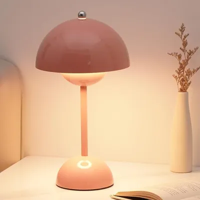 A pink mushroom-shaped LED table lamp sits on a white surface next to a vase with dried flowers.