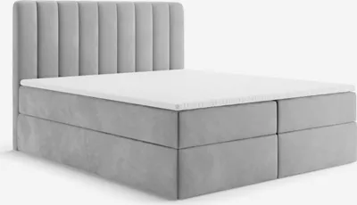 A studio shot of a gray upholstered box spring bed with a white mattress and topper.
