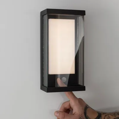 A hand is shown pressing a button on a wall-mounted light fixture.