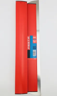 A long, flat metal trowel with a red handle is shown against a white background. Part of the trowel is covered by a red cardboard sleeve with a blue label.
