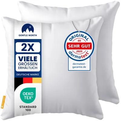 Two white pillows are shown, one slightly behind the other. A label is attached to the front pillow with product information and certifications.
