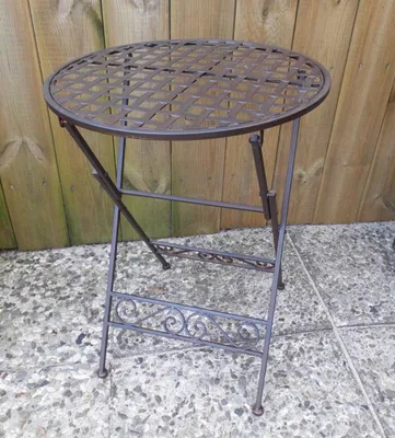 A round, folding metal table with a lattice top is shown outdoors on a patio.