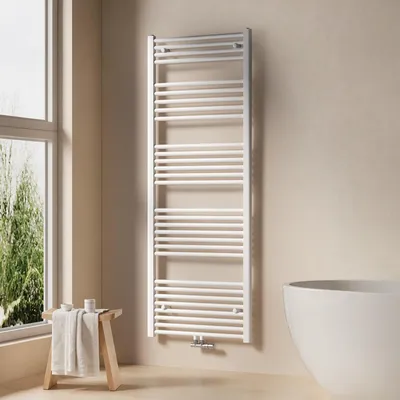 A white towel radiator is mounted on a light beige wall next to a large window. A small wooden stool with a folded towel and some toiletries sits in front of the window.