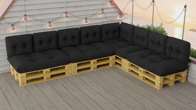 An outdoor patio with a sectional sofa made of wooden pallets and black cushions, decorated with string lights.