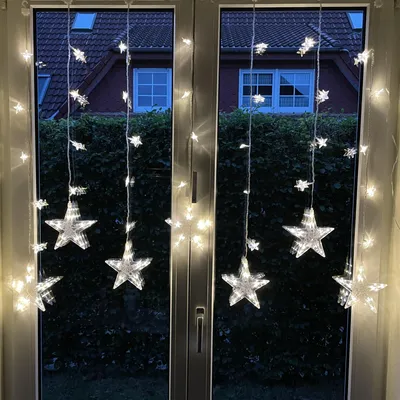 Star-shaped LED string lights hanging in a window at dusk.
