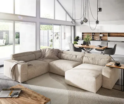 A modern living room with a large sectional sofa, dining area, and kitchen in the background.