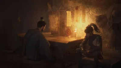Two people are sitting at a desk in a dimly lit room, possibly discussing something.