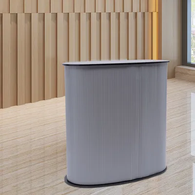 A gray reception desk with a black top sits on a light wood floor in front of a light wood paneled wall.