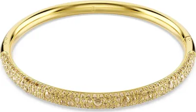 A close-up studio shot of a gold-colored bracelet with small stones embedded in it.