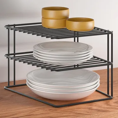 A two-tier corner shelf unit holding plates and bowls, placed on a wooden surface.