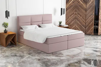 A pink boxspring bed with white bedding is shown in a bedroom setting with a wooden wardrobe in the background.