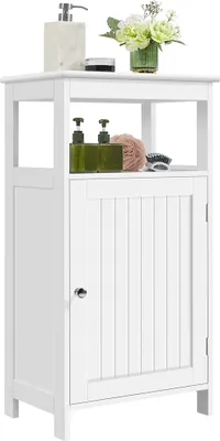 A white bathroom cabinet with a single door and an open shelf above. It is decorated with a soap dispenser, a sponge, and a small vase of flowers.