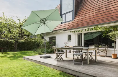 A patio umbrella and outdoor furniture set on a wooden deck next to a house.