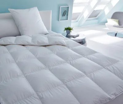 A white duvet is laid out on a bed in a bright, modern room with slanted ceilings and skylights.