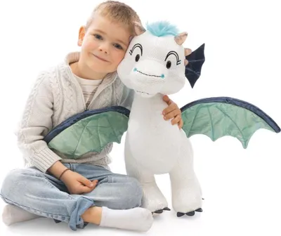 A young boy is sitting on the floor, hugging a plush dragon toy.