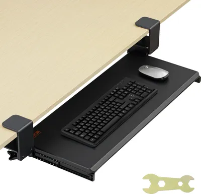 A black keyboard tray with a keyboard and mouse attached, clamped to the underside of a wooden desk.