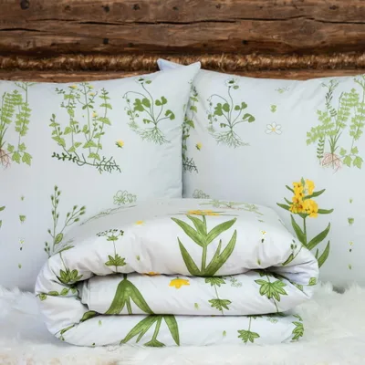 A folded duvet and two pillows with a botanical print are arranged on a white fluffy surface in front of a wooden headboard.