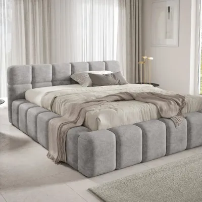A modern, upholstered bed with a tufted headboard and base, set in a softly lit bedroom with sheer curtains.