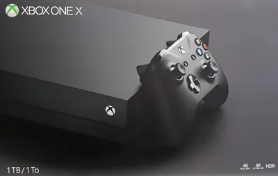 A black Xbox One X console with a controller on top, set against a dark background.