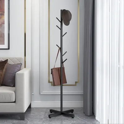 A modern coat rack with a hat and a bag hanging on it, placed in a living room next to a sofa.