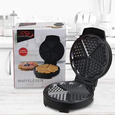 A black waffle maker is shown open, with its cooking plates visible. Next to it is the product's packaging, which also features images of the waffle maker and waffles.