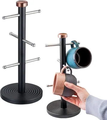 Two black mug trees with copper tops, one empty and one with two mugs hanging on it, with a hand placing a mug on one of the hooks.