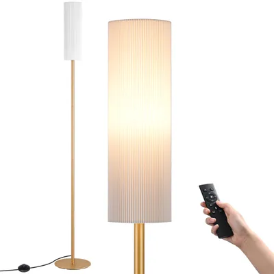 A hand holding a remote control near a floor lamp.