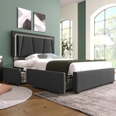 A bedroom scene with a bed as the main focus, featuring storage drawers and a modern headboard with integrated lighting. Large windows with greenery visible outside suggest a natural, airy setting.