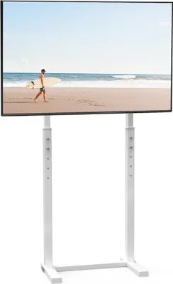 A man walks on a beach carrying a surfboard, with the ocean and sky in the background. The image is displayed on a white TV stand.